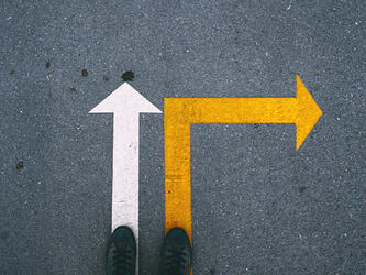 feet pointing at a white arrow pointing straight ahead and a yellow arrow pointing right on a pavement